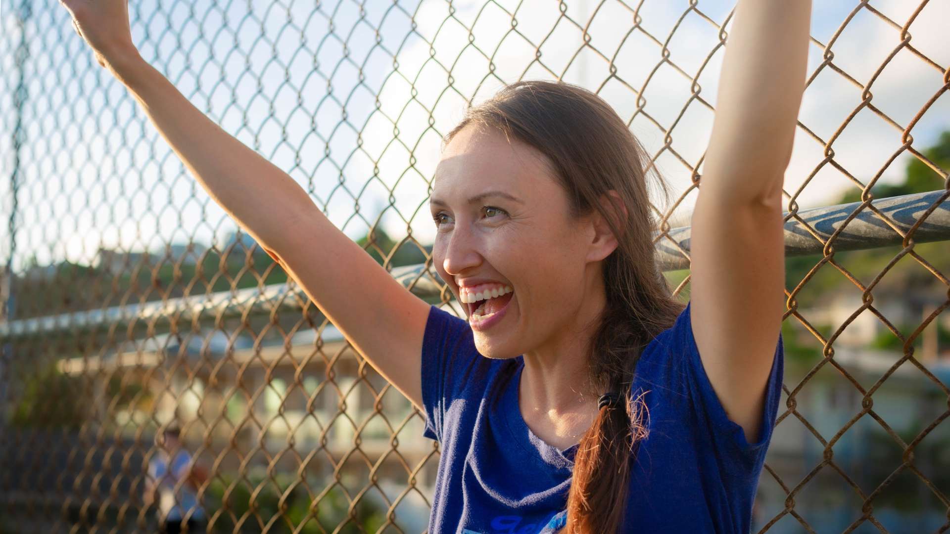 A baseball team mom cheering for the kids with a big smile on her face and her arms raised above her head.