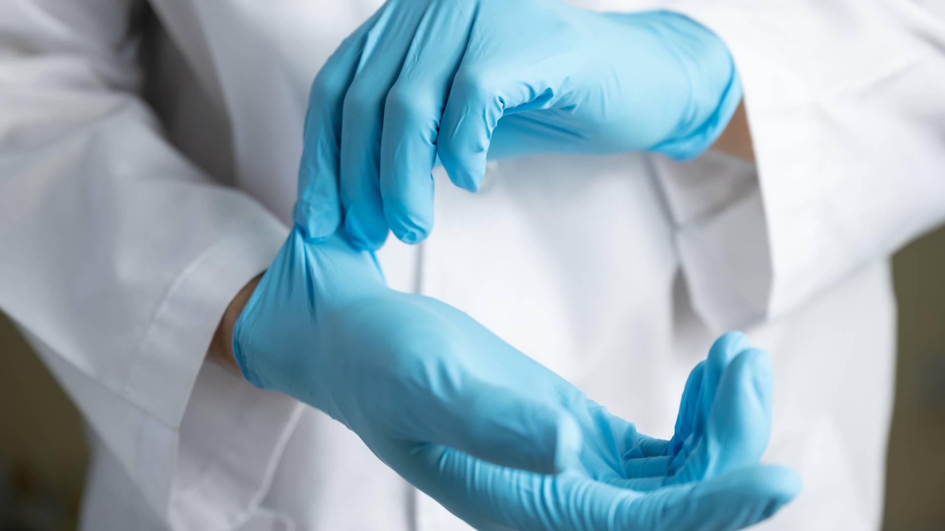 A healthcare lab professional putting a pair of sterile nitrile gloves on their hands. They're also in a white lab coat.