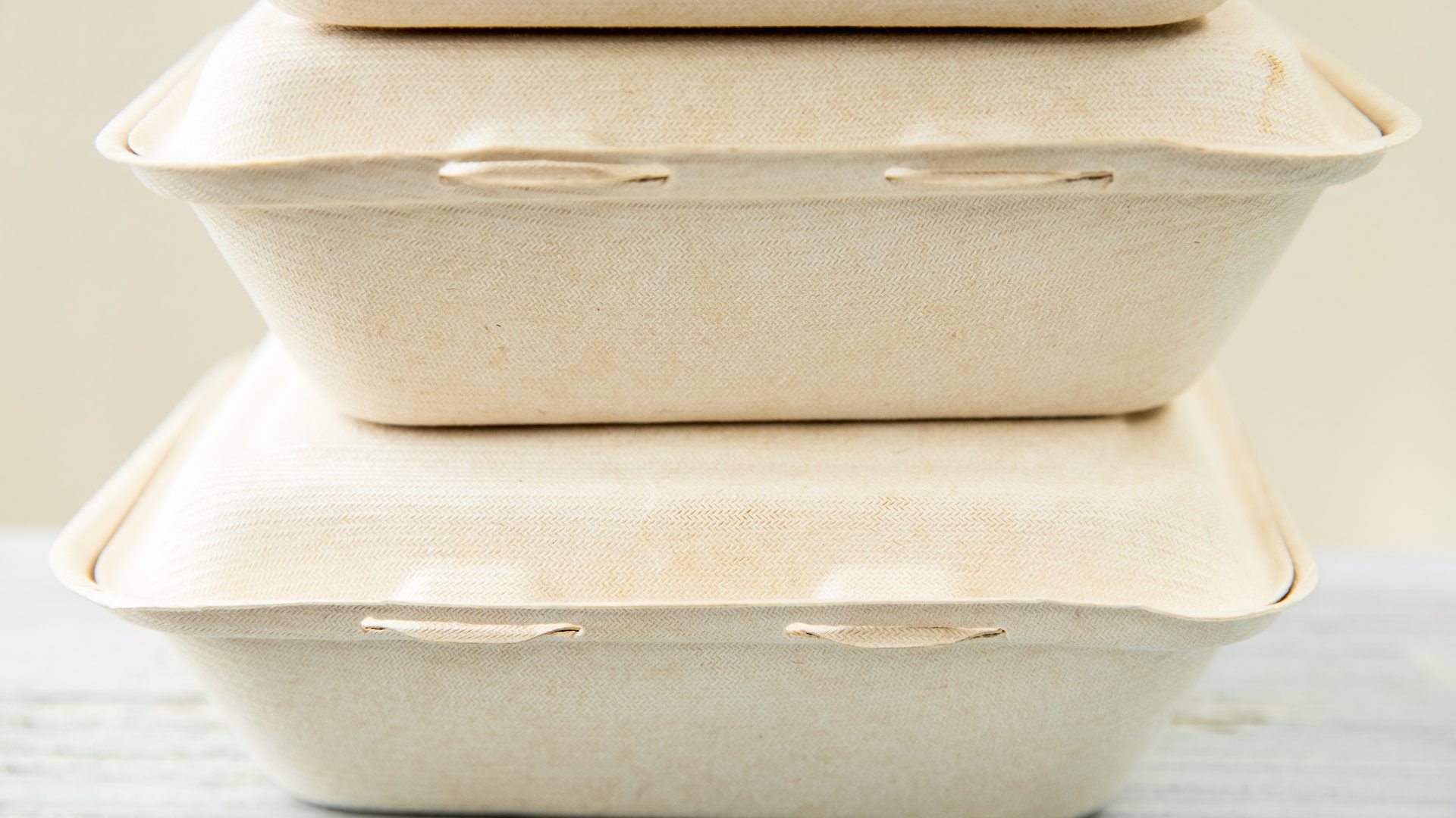 A stack of three recyclable food takeout containers sitting on a table. They containers are eco-friendly.