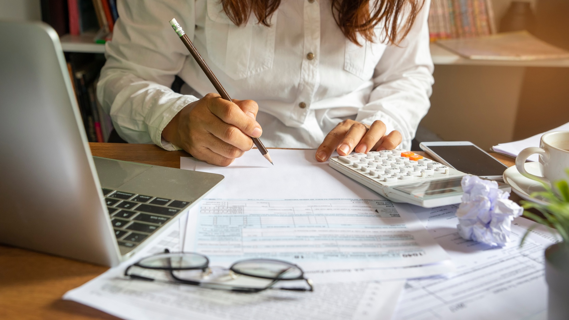 A business owner sitting at a desk in an office and going over financial documents and tax forms with a calculator.