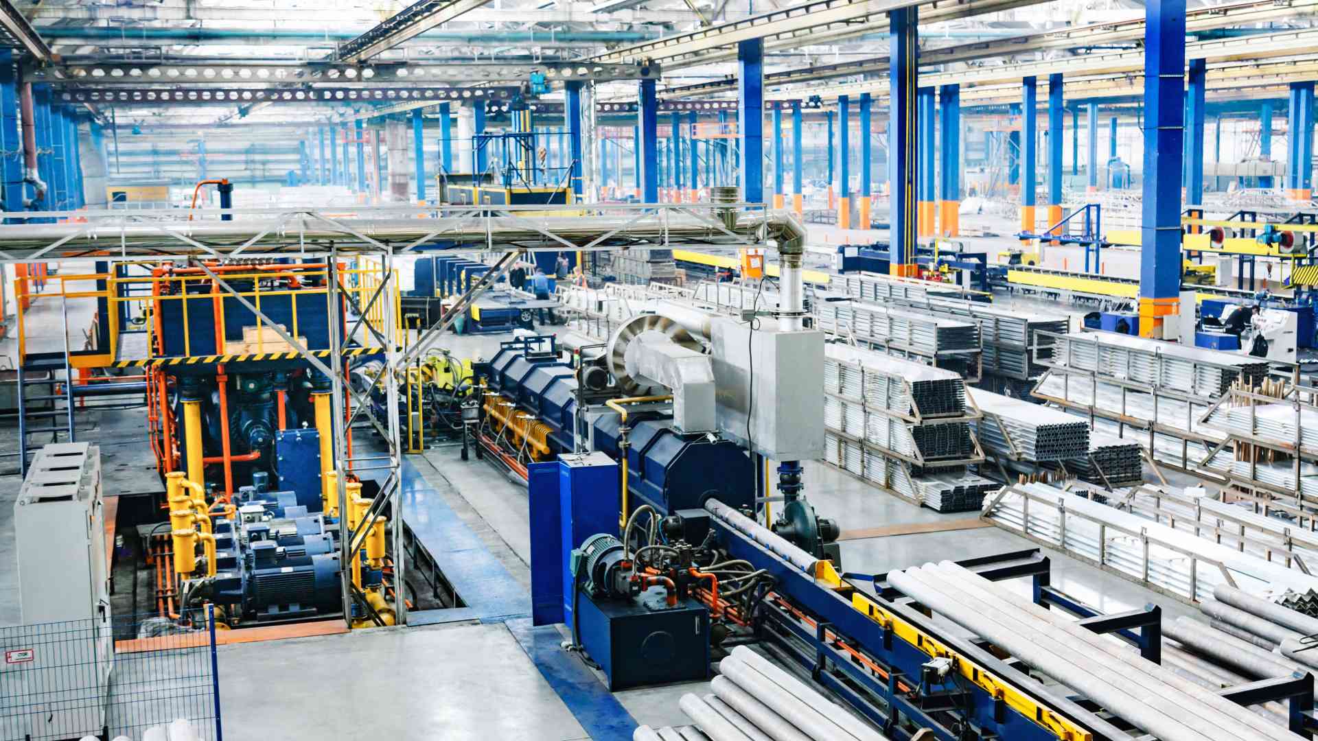 A large business warehouse is full of different machines and industrial materials, with some orange and blue poles.