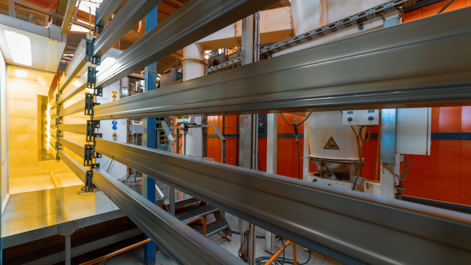 Extended molded pieces of metal being coated and cured with yellow powder coating on an assembly line.