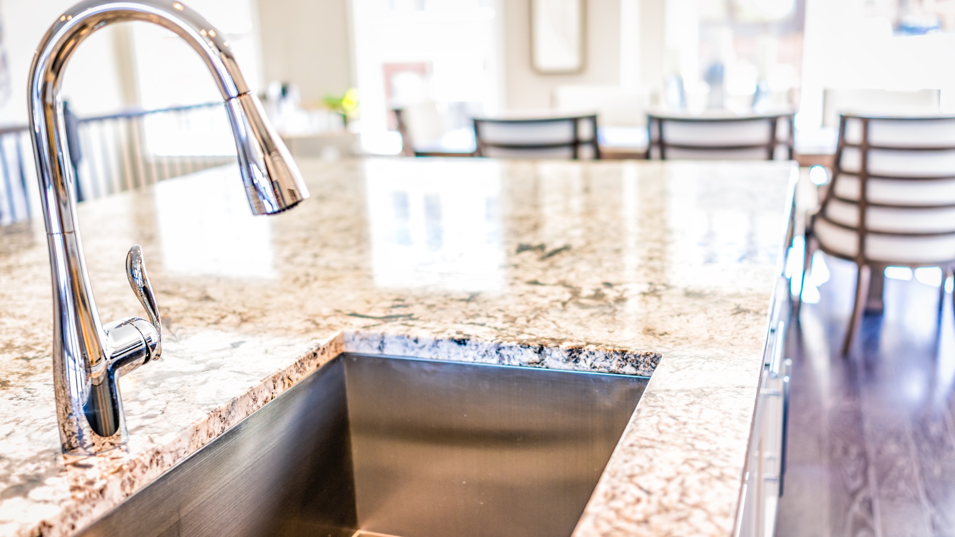 A close-up of a kitchen island with a drop-in stainless steel sink and light colored granite countertops.