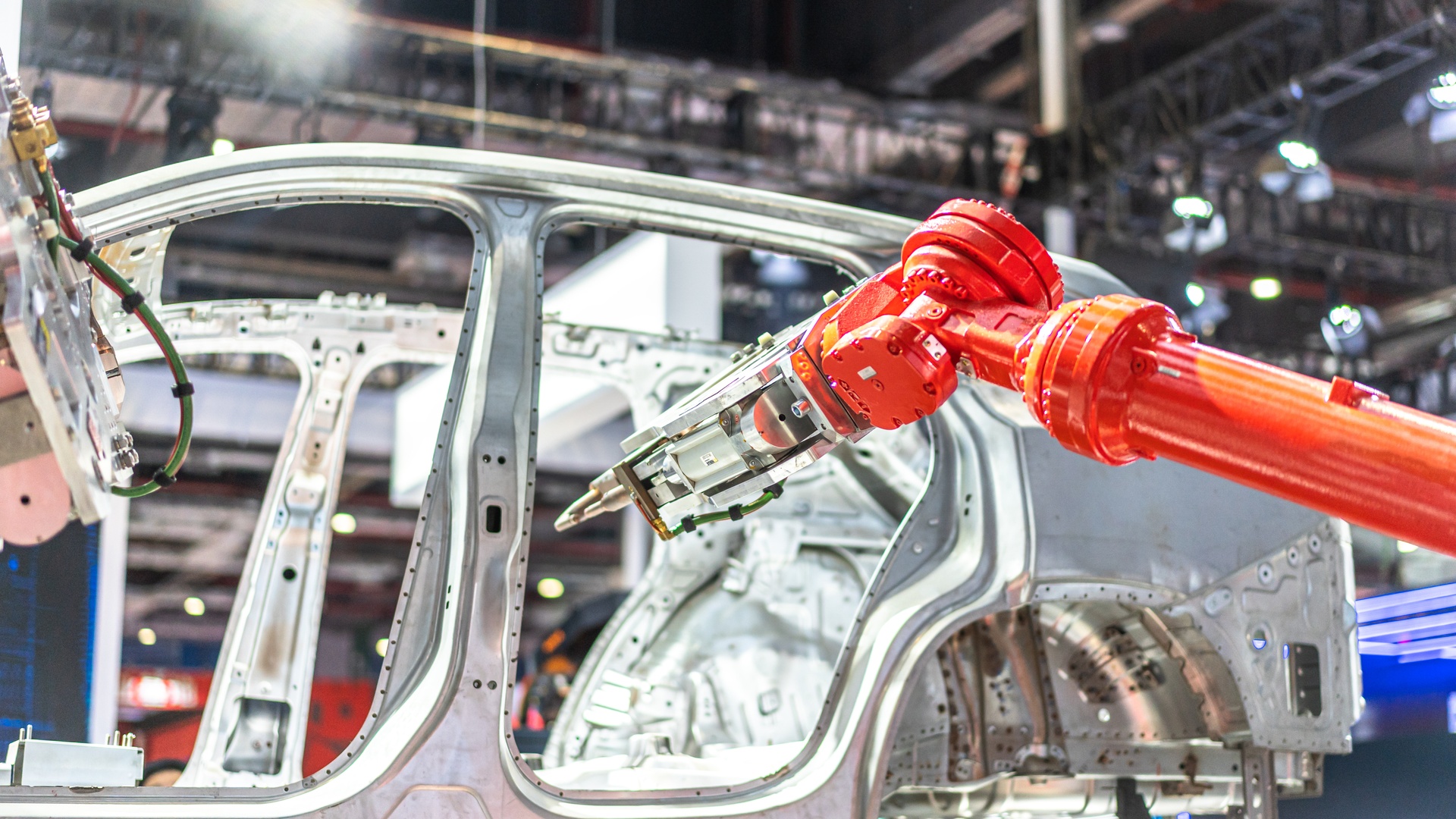 A low-angle view of a robotic arm hovering near the metal frame of a vehicle on a factory production line.