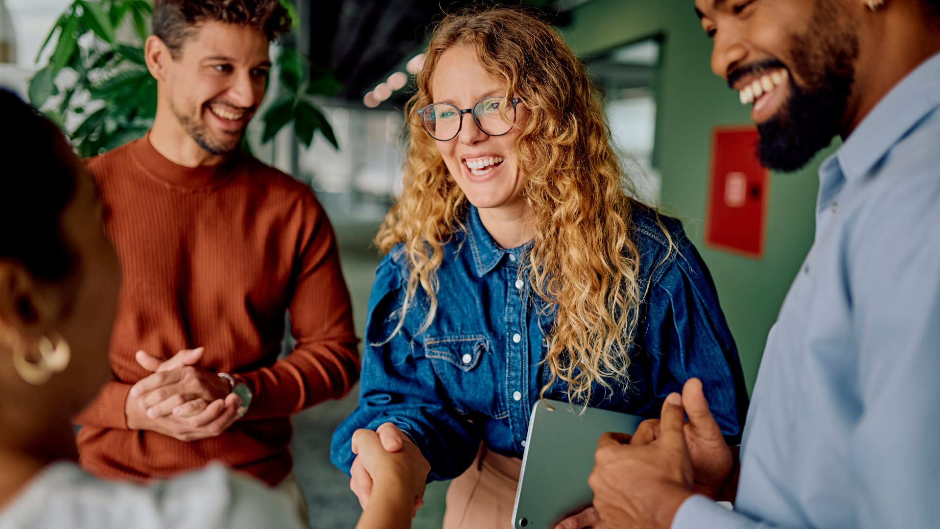 A group of employees stand together as the new female employee shakes the leaders hand with a smile on her face.