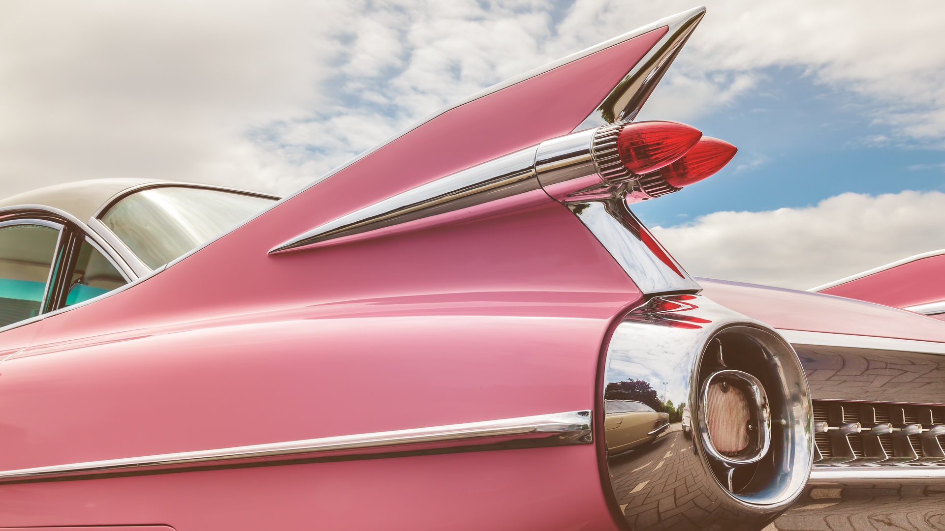 An up close view of a classic car's rear taillight. The classic car is bubblegum pink with silver trim and details.