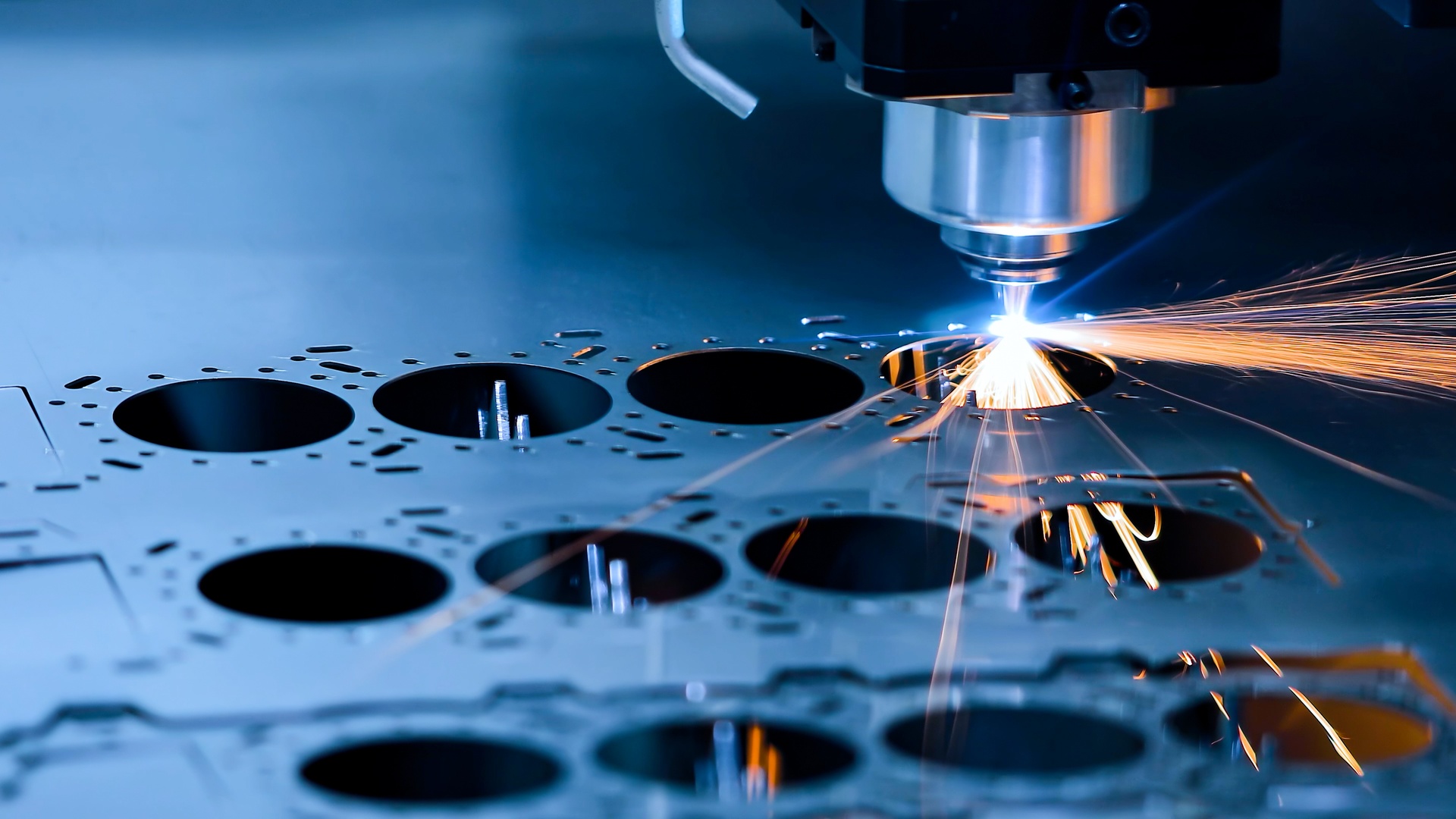 A CNC milling machine cuts a circle into a thin metal sheet, emitting orange sparks from the cutting point.