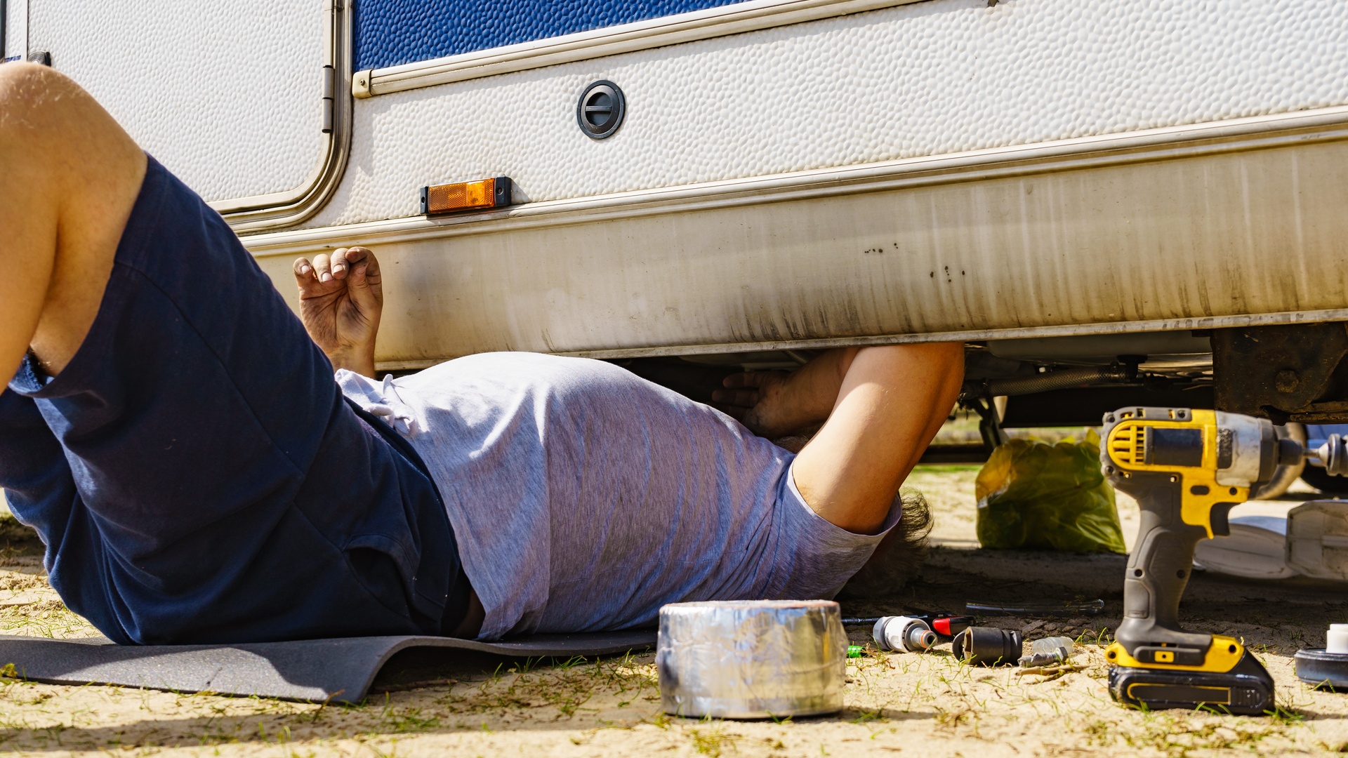 A man laying on the ground underneath his RV. He has some tools on the ground next to him as he works on the vehicle.