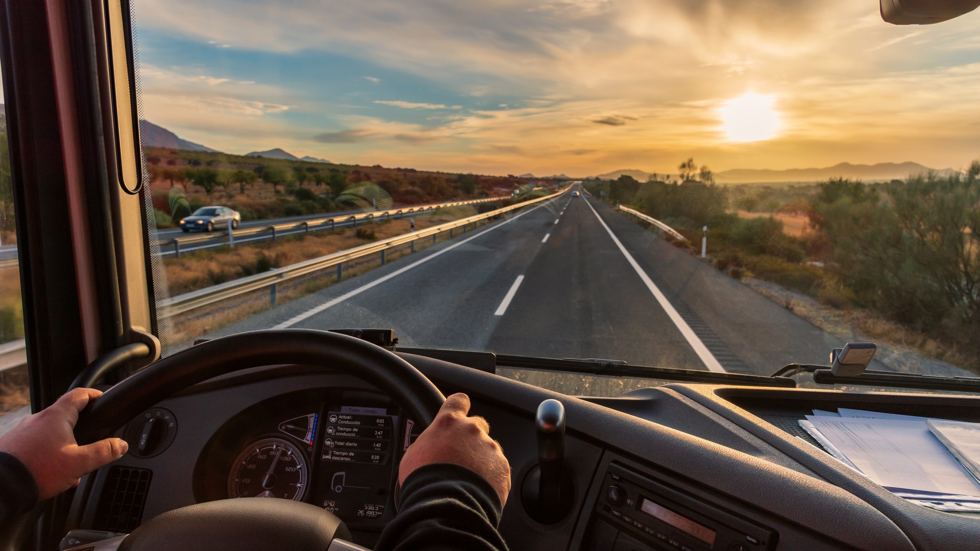 The view of the open road from a truck driver's perspective. The sun sets around the beautiful mountainous environment.