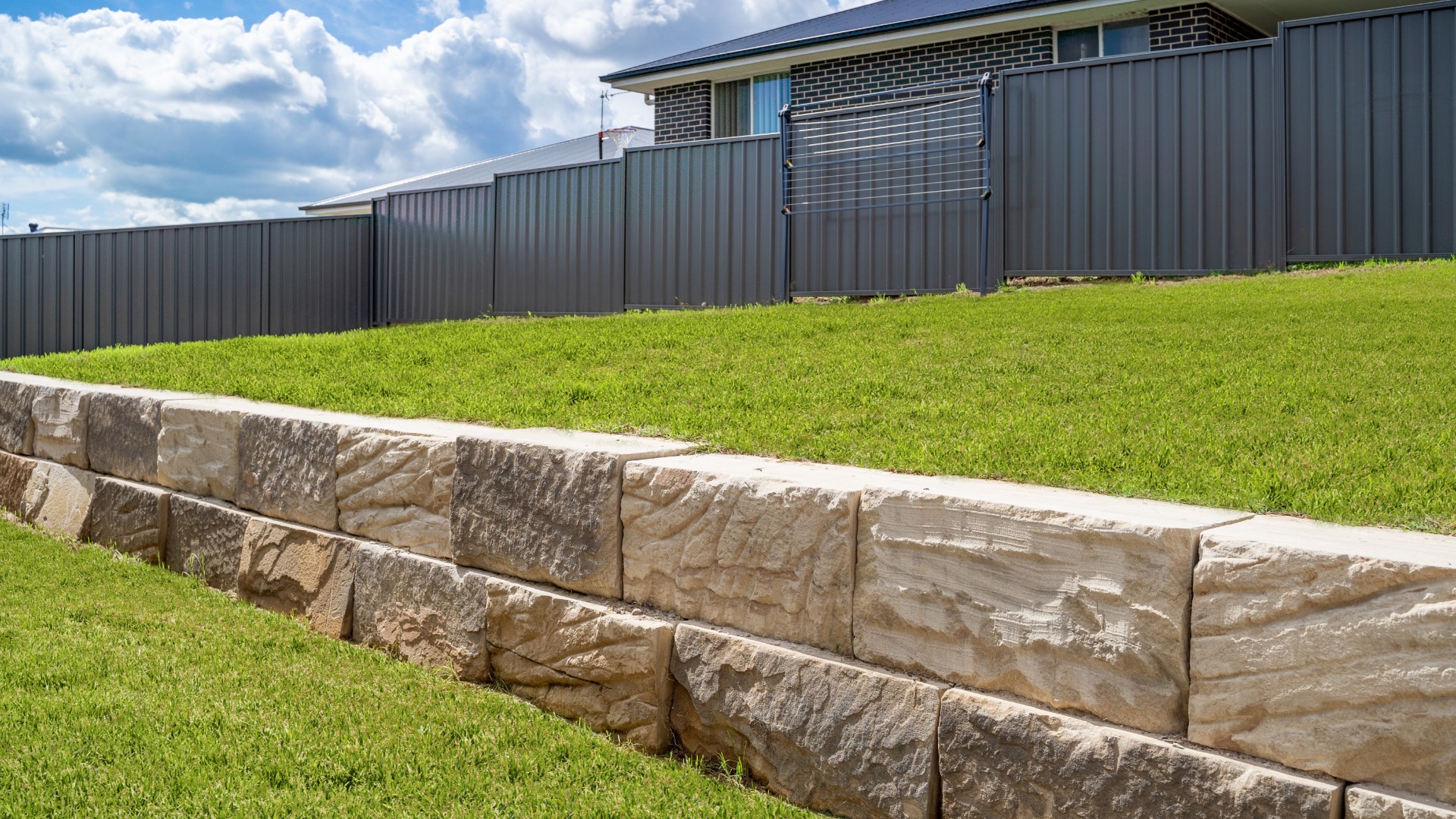 A stone retaining wall built into a hill of a backyard. The grass is well-maintained and there's a fence in the distance.