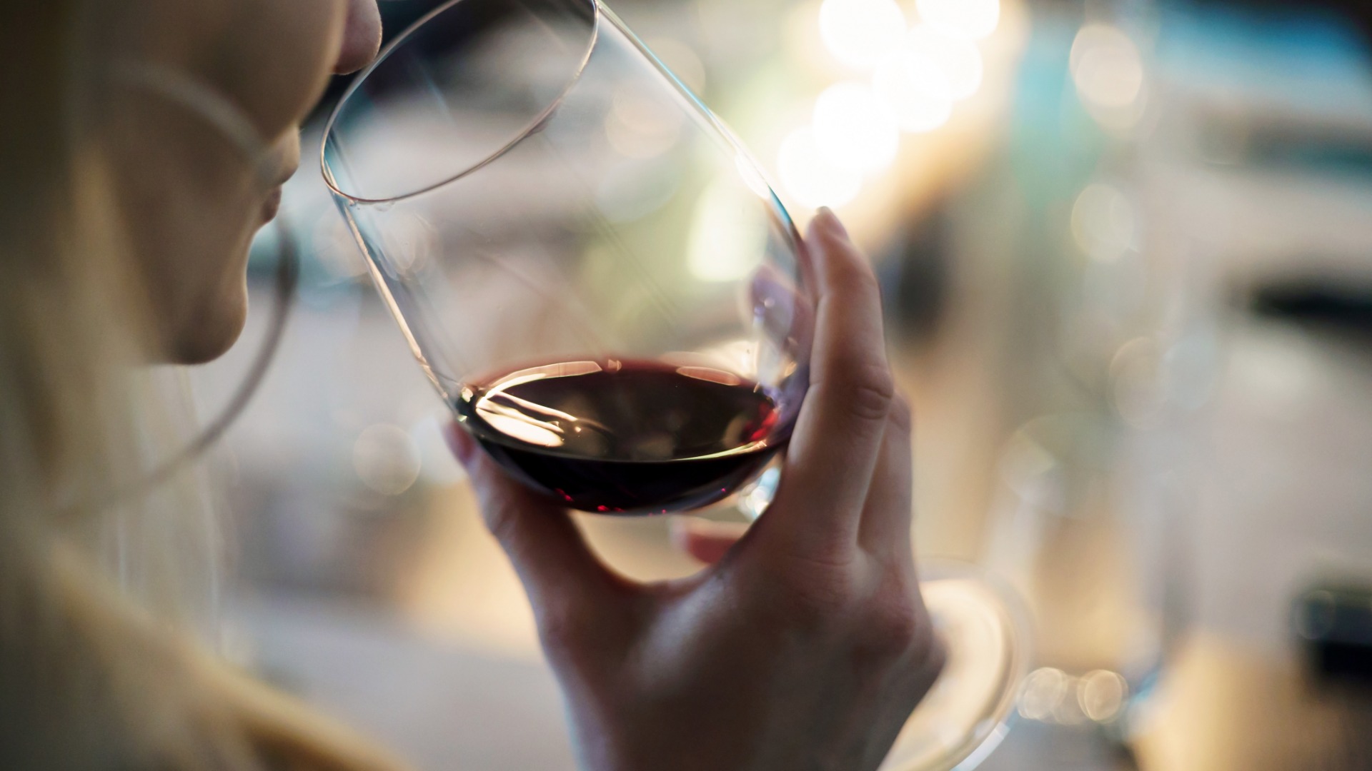 A person holding a glass of wine to their mouth while sitting at a table during a wedding. The glass has red wine in it.