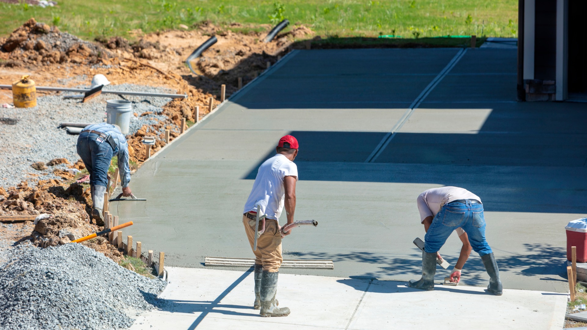 A team of three workers in a construction zone outside of a home. The workers are installing a driveway.
