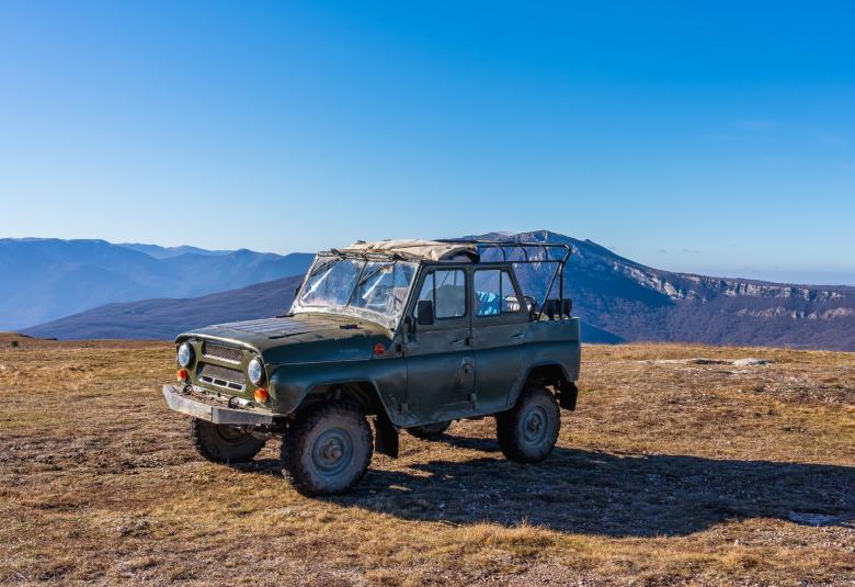 An old vintage Jeep finished in a classic forest green color parked in a grassy field atop a mountain.