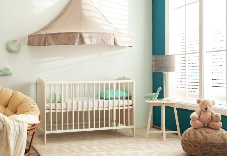 A baby's nursery. It features a crib with an overhead canopy, a bowl chair, a side table, and a large window lighting everything.
