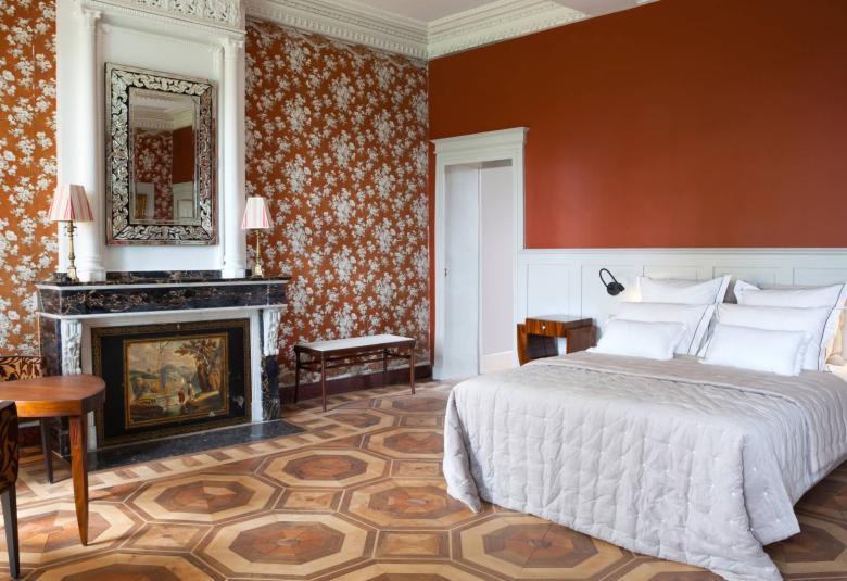 A bedroom decorated with varying patterns of burnt orange designs on the walls and floor with white, vintage crown molding.