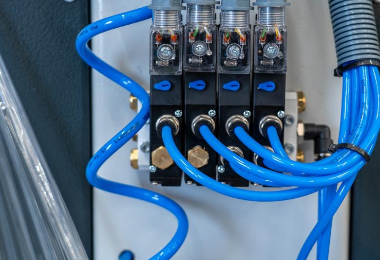Solenoid valves with four black control blocks, transparent wiring, and blue tubing connected in sequence.