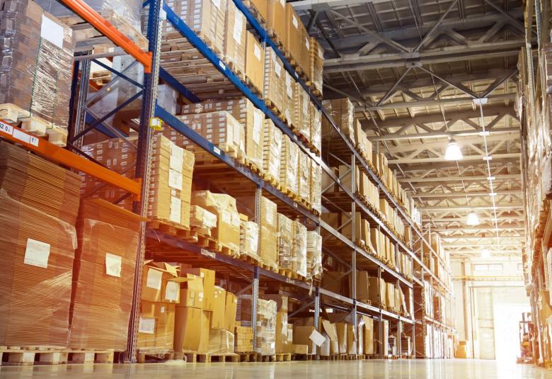 A row of shelves in a warehouse with different products stored on the tall shelves. Some are in packaged boxes.