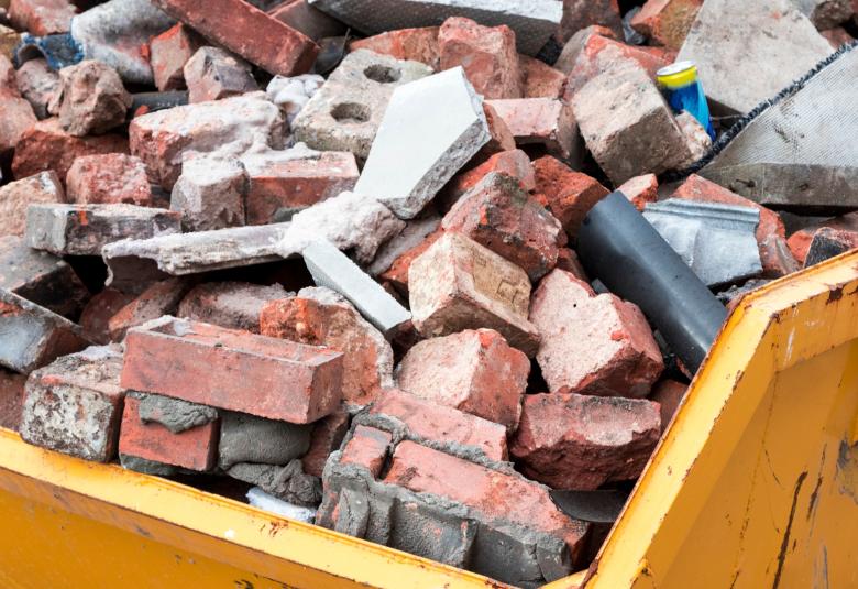 A yellow dumpster full of bricks and other construction waste materials.