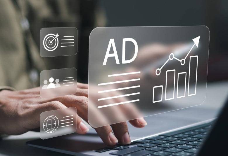 A graphic box featuring the word "AD" next to an ascending bar chart hovers above a laptop in front of a blurred man.