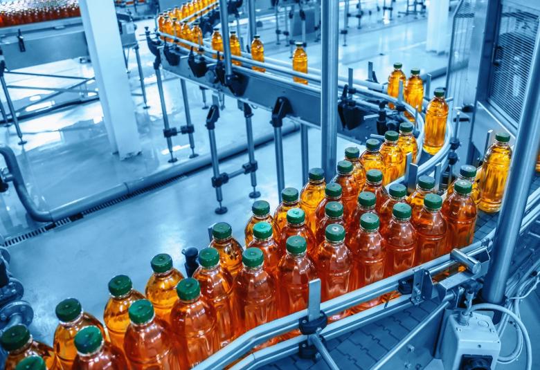 Hundreds of bottles of an amber-colored beverage move through a manufacturing facility on a conveyor system.