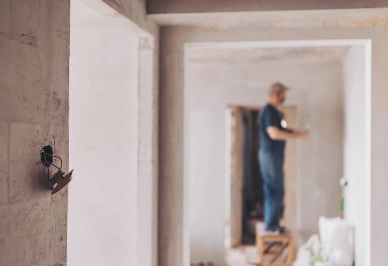 A wall in a building is under construction, with visible scaffolding and a worker wearing a hard hat in the background.