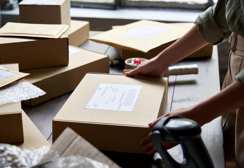A person with rolled-up sleeves is placing their hands on a rectangular cardboard box that is sitting on a table.