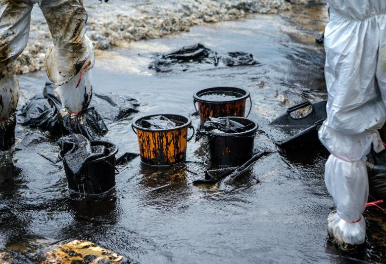 Two crew members wade an oil spill in protective gear as they use four buckets to begin recovery cleanup.