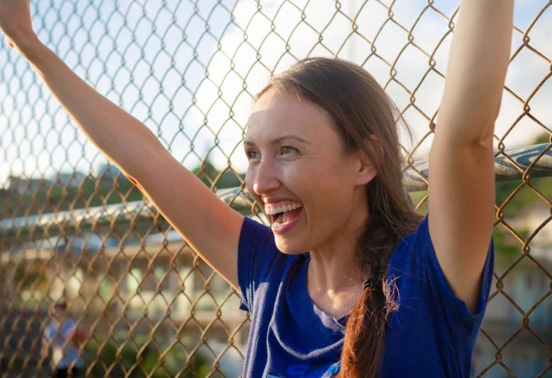 A baseball team mom cheering for the kids with a big smile on her face and her arms raised above her head.