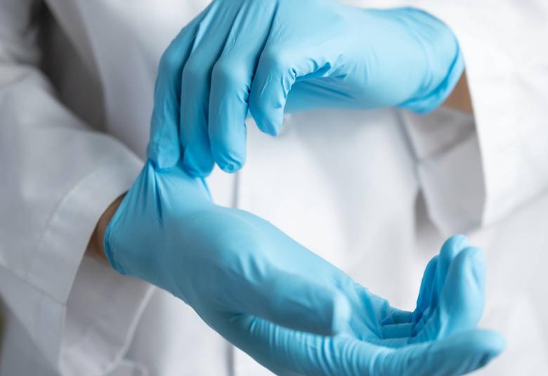 A healthcare lab professional putting a pair of sterile nitrile gloves on their hands. They're also in a white lab coat.