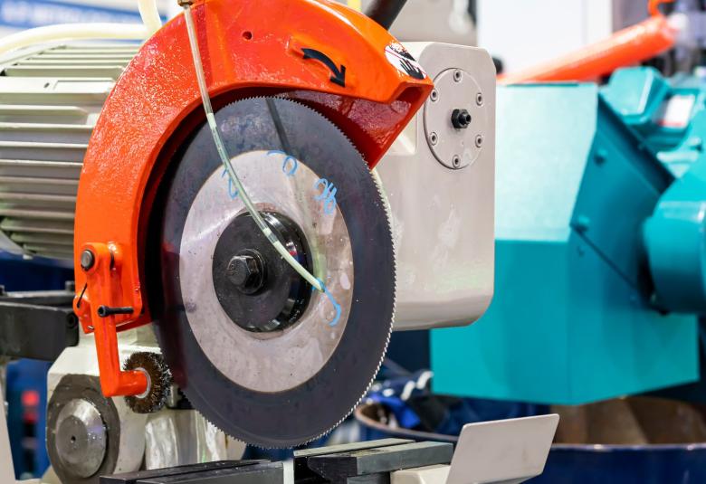 A close up of a cold saw machine sitting in an industrial work facility. It's next to other industrial machines.