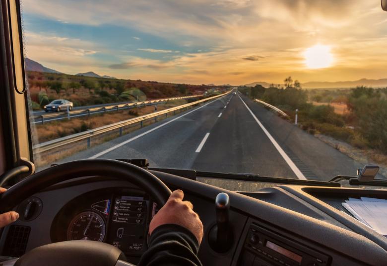 The view of the open road from a truck driver's perspective. The sun sets around the beautiful mountainous environment.